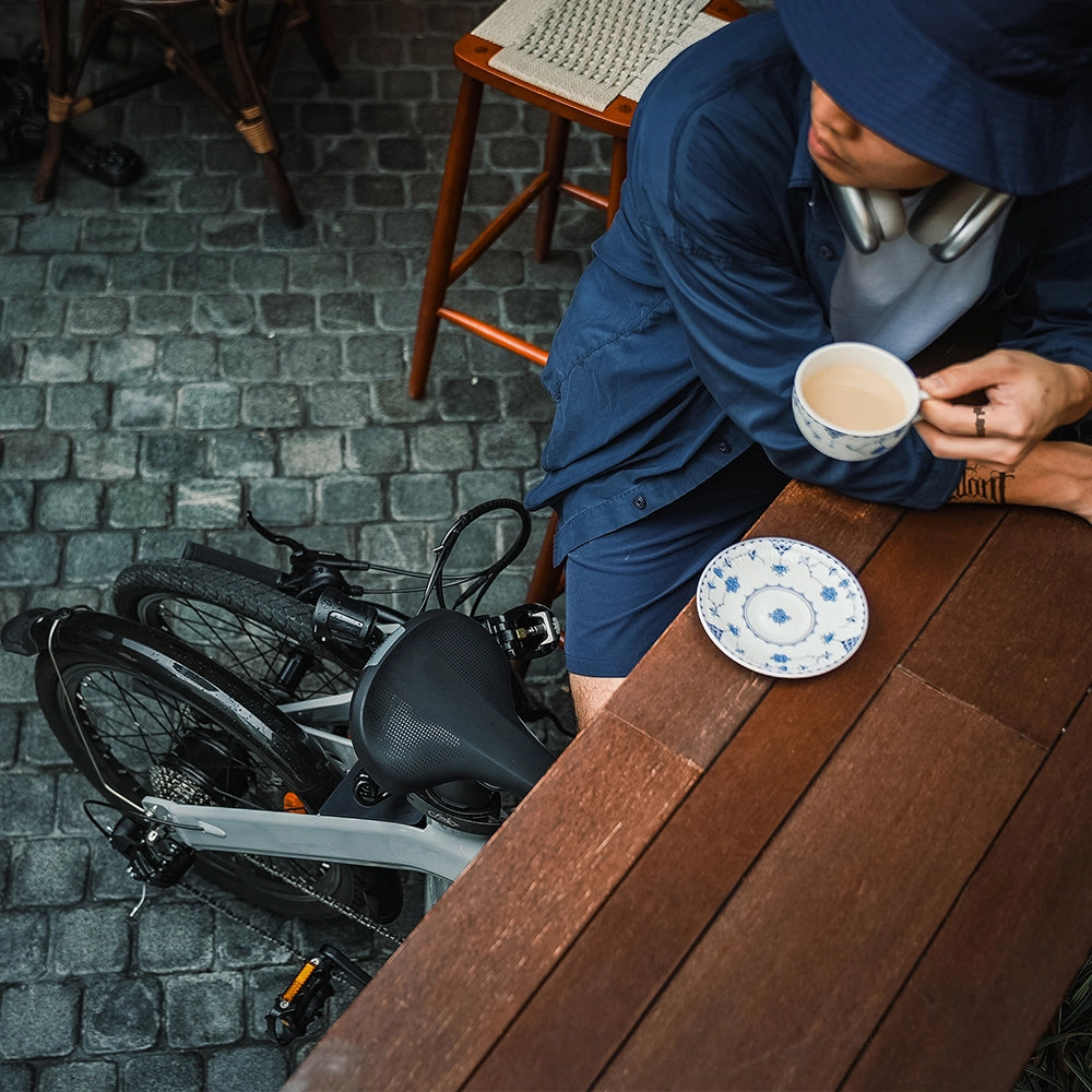 Henkilö istumassa kahvilassa. Henkilöllä on mukanaan taitettava sähköpyörä.