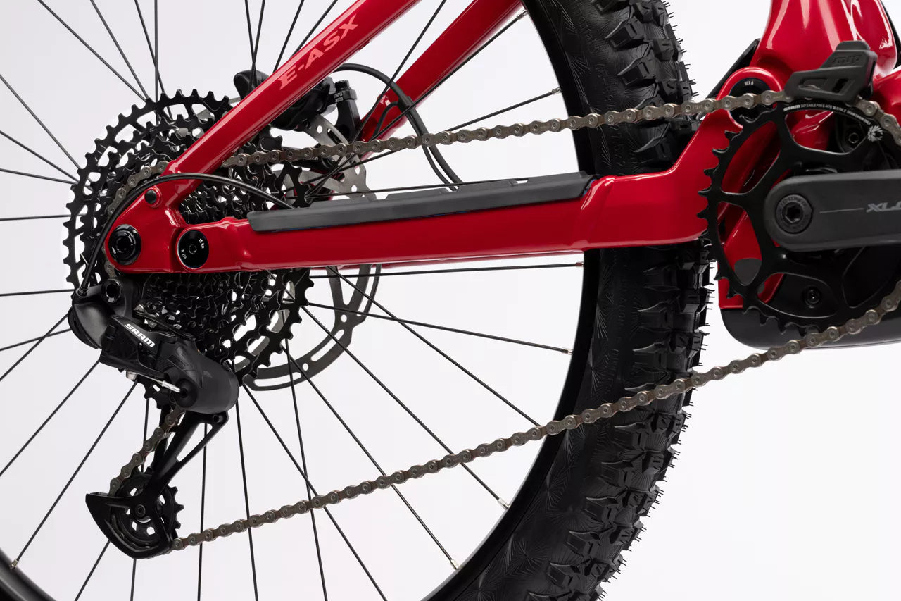 Lähikuva SÄHKÖPYÖRÄT.NETin punaisen Ghost E-ASX Essential 2026 -mallin takapyörästä, vaihteista ja ketjusta, jossa korostuvat Bosch Performance Line CX -mallin voimansiirto ja renkaan kulutuspinnat valkoista taustaa vasten.