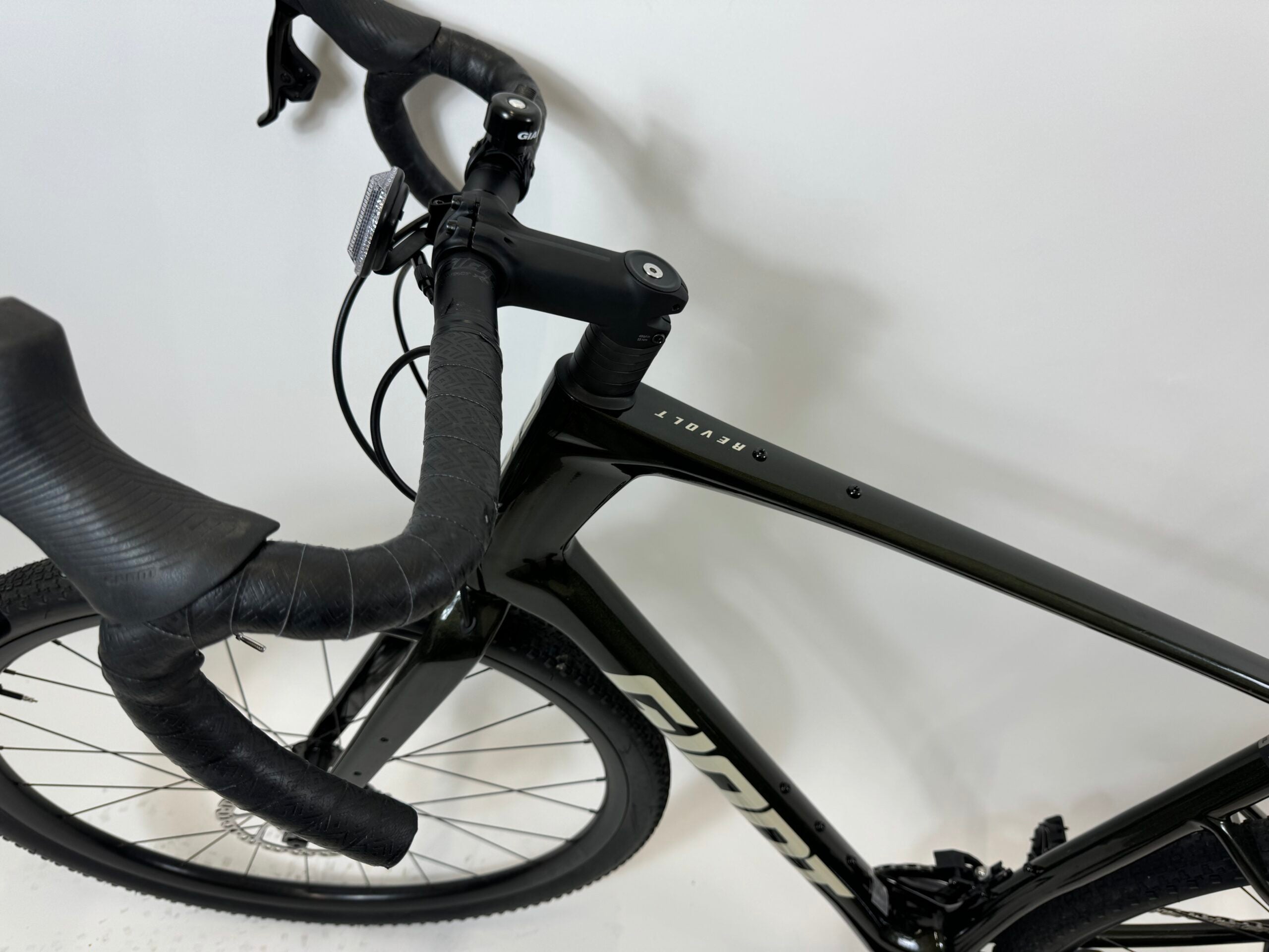 Lähikuva mustasta Giant Revolt Advanced 1 Käytetty gravelpyörä päässä SÄHKÖPYÖRÄT.NET, asetettu valkoista taustaa vasten, korostaen ohjaustanko, etupyörä, ja hiilikuiturunko yläputki merkitty "SECRET.