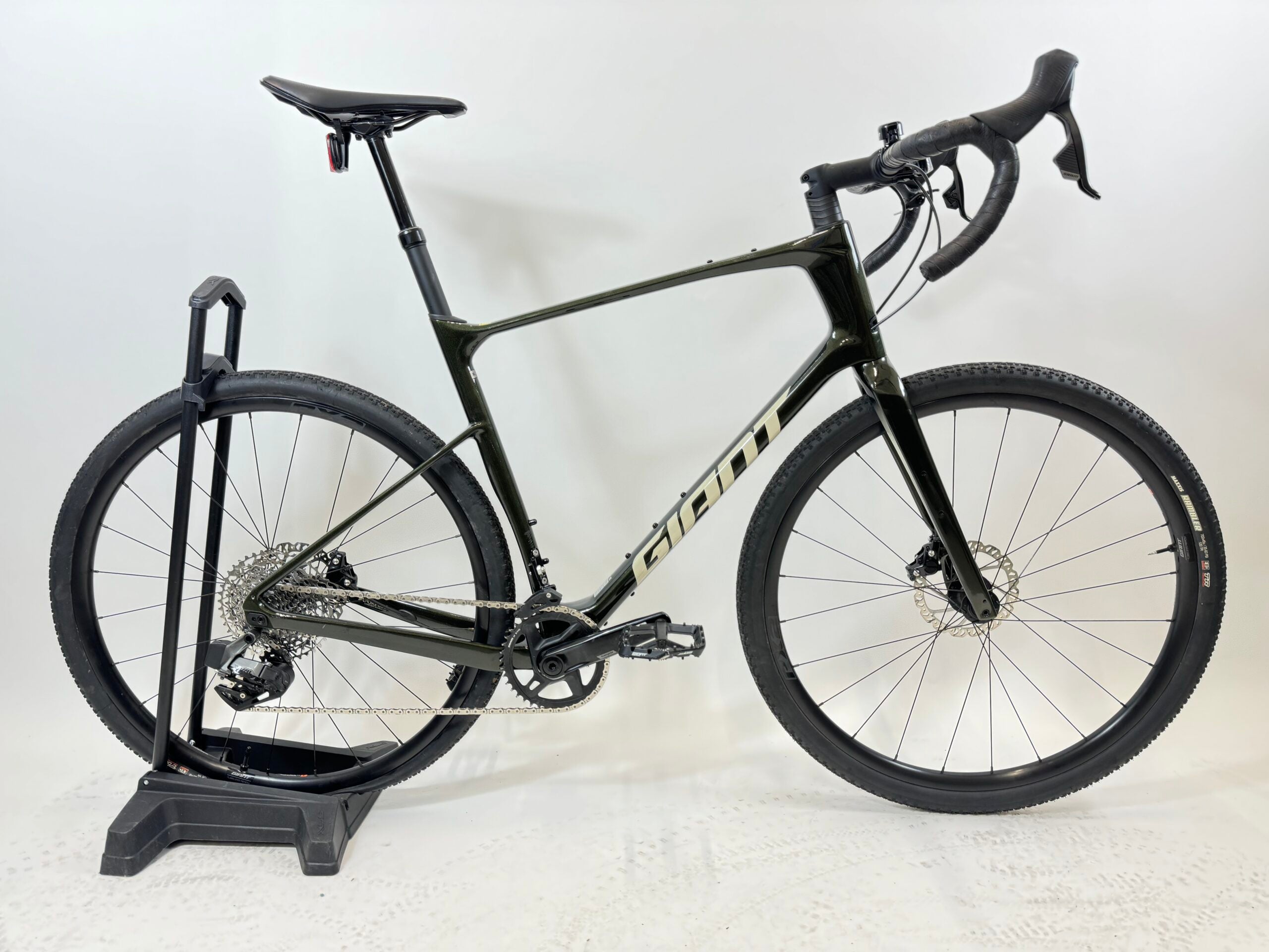 SÄHKÖPYÖRÄT.NETin musta Giant Revolt Advanced 1 Käytetty gravelpyörä, jossa on drop-ohjaustanko, levyjarrut ja tyylikäs hiilikuiturunko, on esillä jalustalla valkoista taustaa vasten.