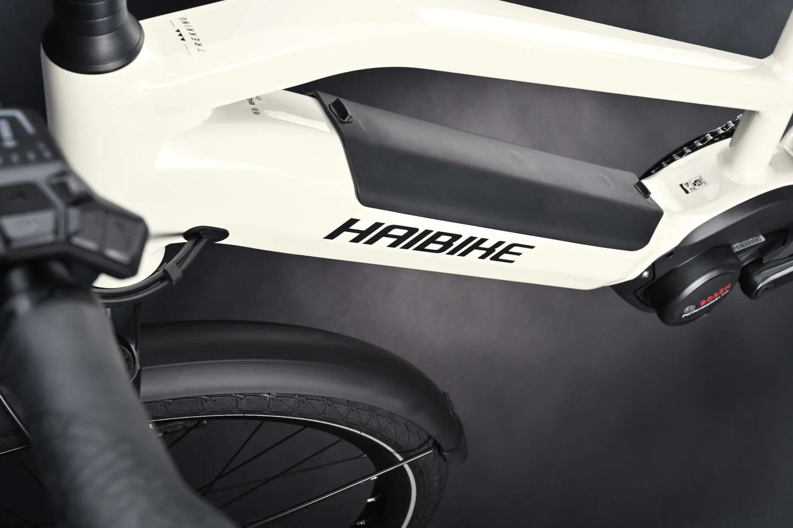 Lähikuva valkoisesta Haibike TREKKING 3 High S-koko by SÄHKÖPYÖRÄT.NET -mallista, jossa näkyy runko, Bosch Performance -akku, osittainen ohjaustanko ja takapyörä tummaa taustaa vasten.