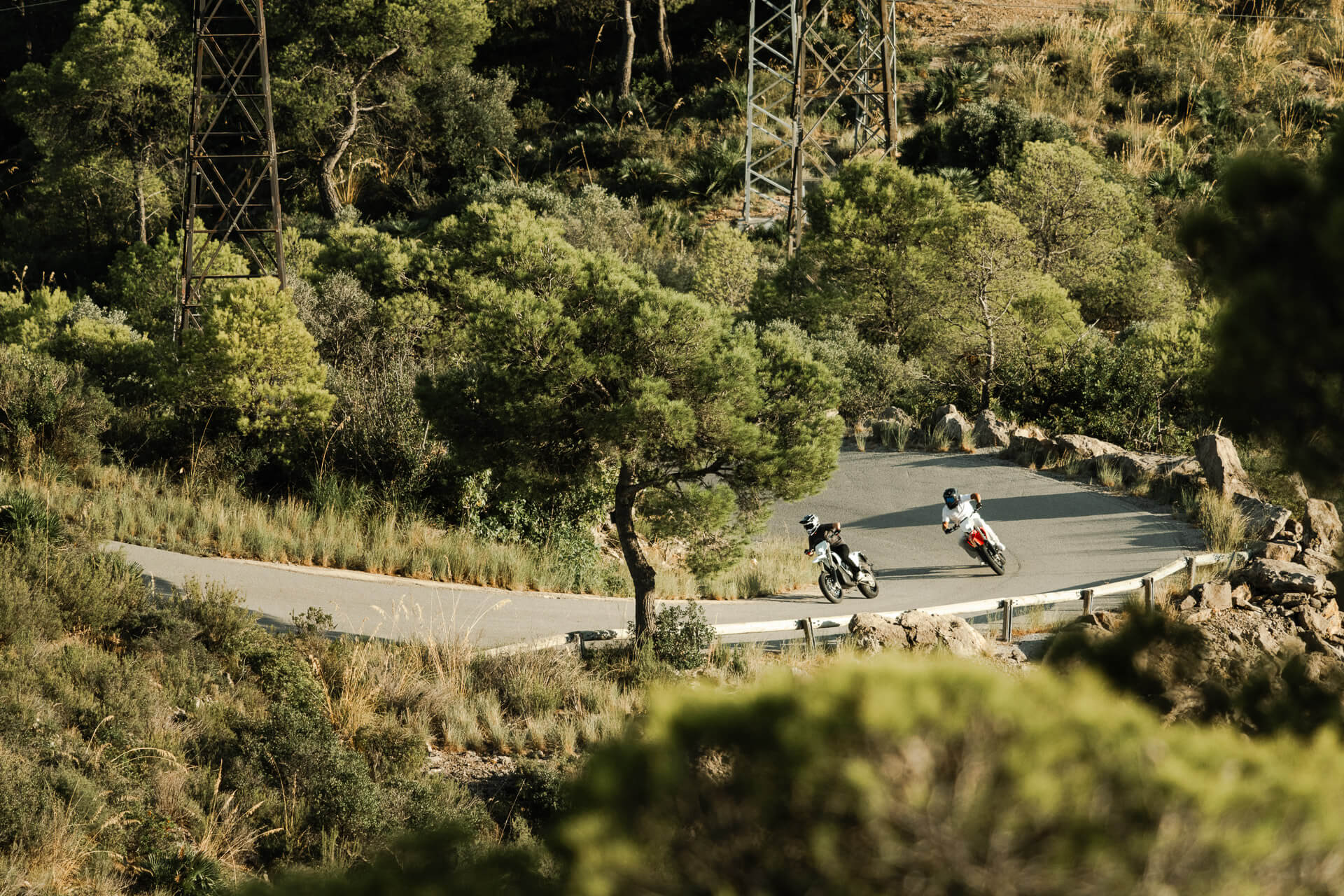 Kaksi kuljettajaa ajelee Stark Varg SM *korkotarjous alkaen 1,99 %* sähkömoottoripyörillään Starkilla pitkin mutkaista metsätietä, jota ympäröivät korkeat puut ja kallioiset kukkulat aurinkoisena päivänä.