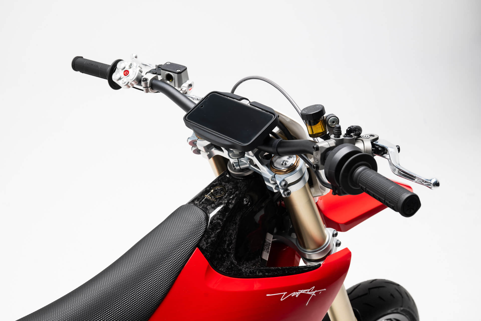 Stark Varg SM *korkotarjous alkaen 1,99 %* lähikuva: supermoto-ohjaustanko, digitaalinen näyttö, ohjauspainikkeet, kuvioitu musta istuin. Kirkkaanpunainen sähkömoottoripyörän runko valkoisella logolla ponnahtaa valkoista taustaa vasten.