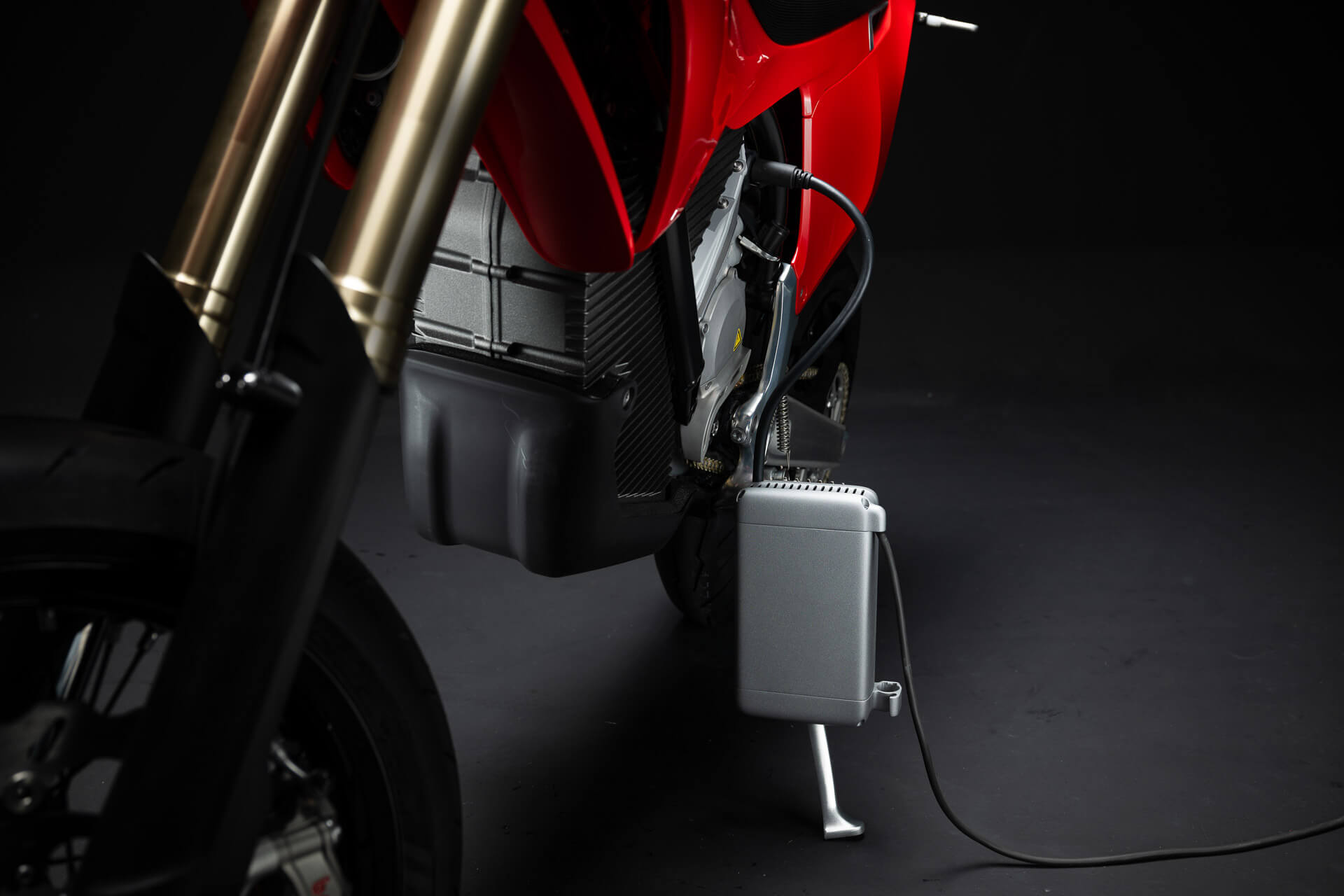 Lähikuva Stark Varg SM *korkotarjous alkaen 1,99 %* sähkömoottoripyörä Starkilta, lataus hopeisella laturirasialla ja kaapelilla tummaa taustaa vasten.