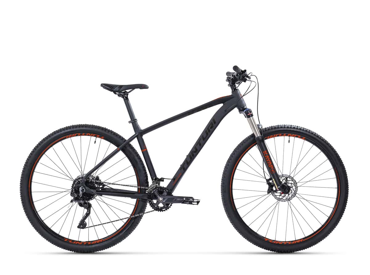 SÄHKÖPYÖRÄT.NETin Tunturi Kayapo 29" on musta ja punainen maastopyörä, jossa on paksu 29" renkaat, etujousitushaarukka, Shimano hydrauliset levyjarrut ja hieman kalteva yläputki, joka näkyy sivulta valkoisella tausta.