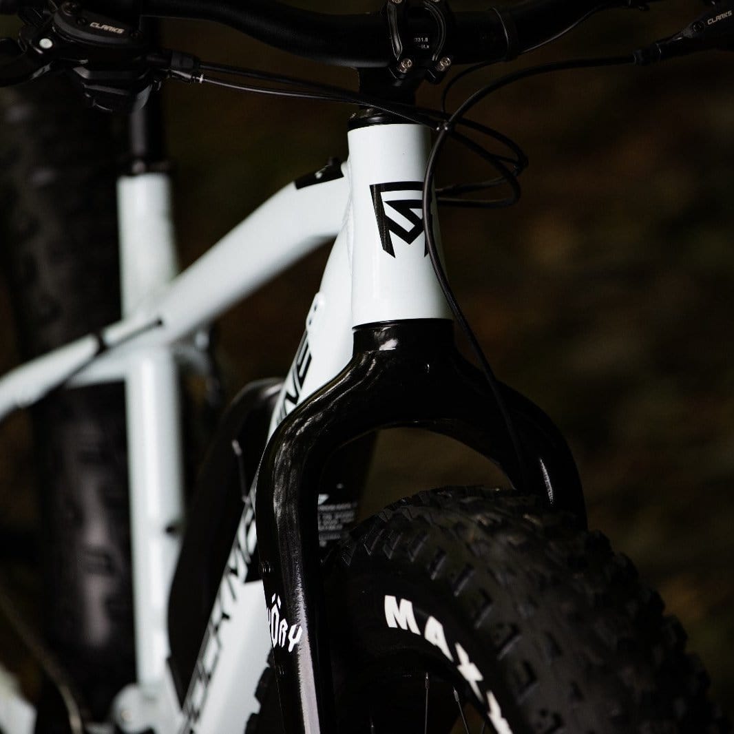 LĂ€hikuva SĂHKĂPYĂRĂT.NETin Rock Machine Vyöry E50R:stĂ€ - valkoisesta e-fatbike-pyörĂ€stĂ€, jossa on ohjaustanko, etuhaarukka, paksu Maxxis-rengas, geometrinen musta logo rungossa ja Shimano EP6 -moottori, joka parantaa suorituskykyĂ€.