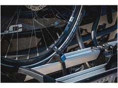 Lähikuva sähköpyörän pyörästä, joka on kiinnitetty Thule XLC Azura Xtra VC-10 pyöränkuljetustelineeseen, taitettava ja lukittava, sekä yksityiskohtia renkaasta, telineestä ja ajoneuvon osasta taustalla.