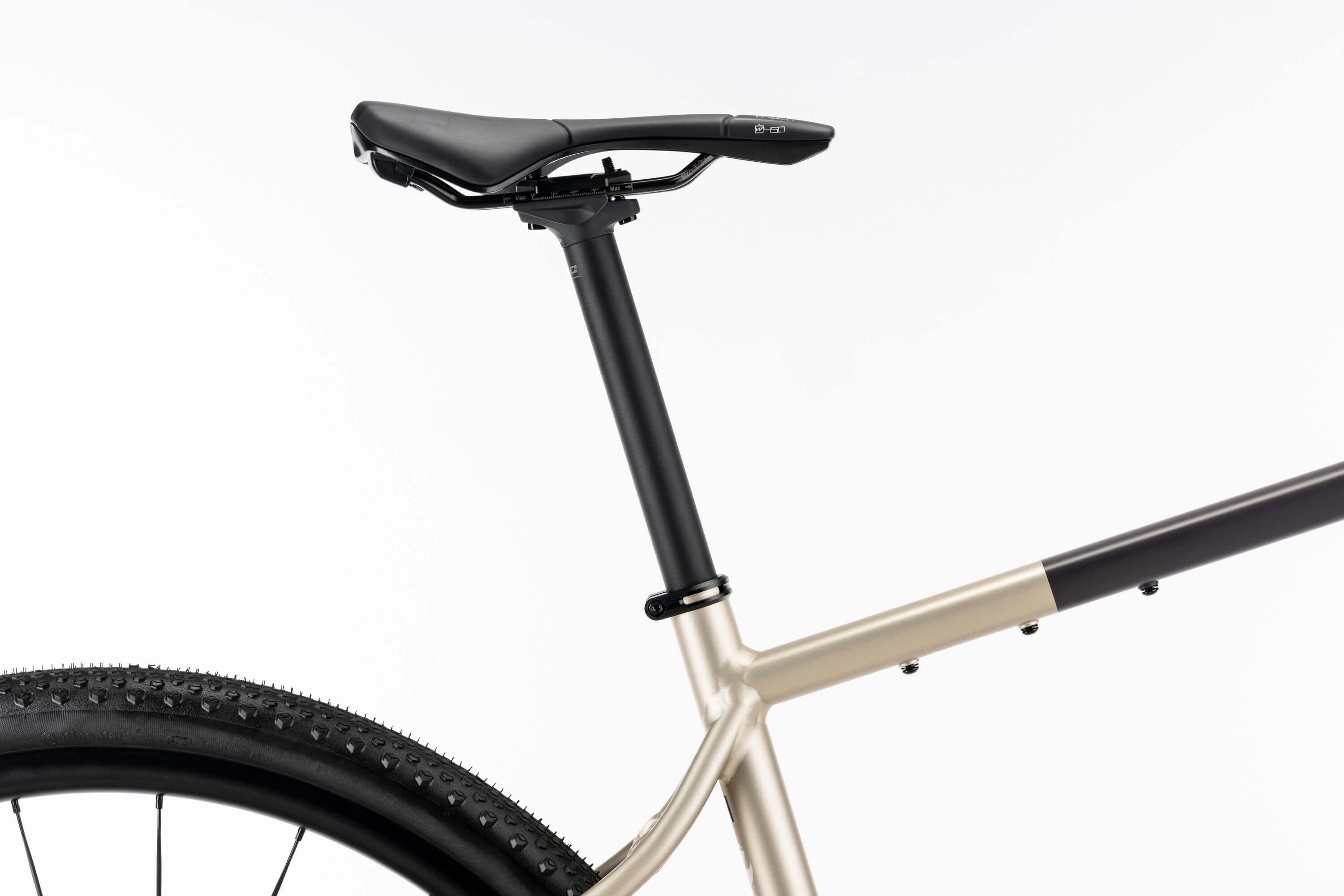 Lähikuva Ghost Asket Advanced -gravelluspyörästä, jossa näkyy sen satula, istuinpylväs ja metallinen runko. Osa takapyörästä näkyy valkoista taustaa vasten, ja Shimano GRX -komponentit tarjoavat ensiluokkaiset yksityiskohdat.
