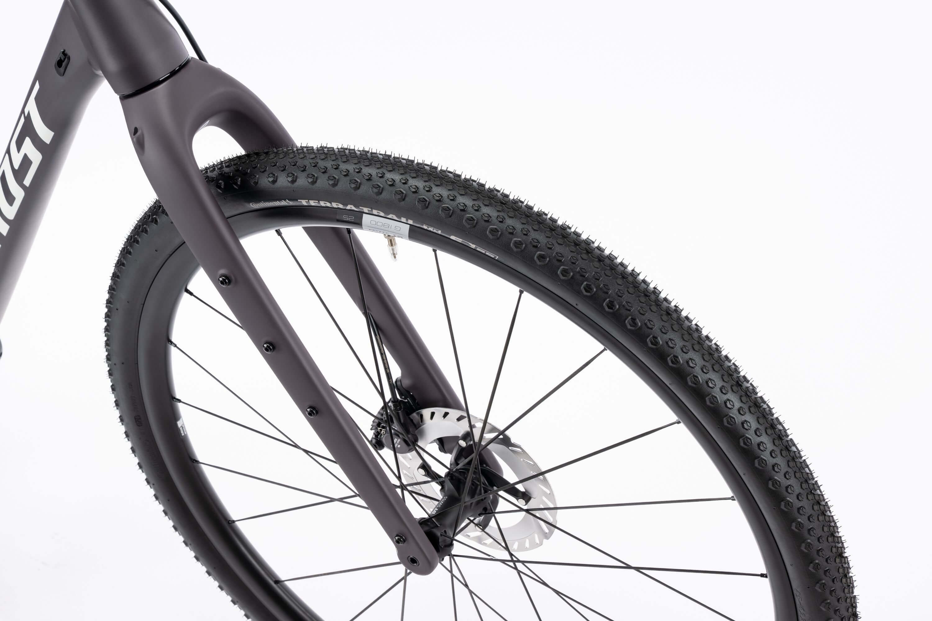 Lähikuva Ghost Asket Advanced -sorapyörän etupyörästä, jossa on nupukoitu rengas, mustat pyöränkehät, Shimano GRX -levyjarru ja Ghostin mattamusta haarukka valkoista taustaa vasten.