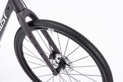 Lähikuva Ghost Asket Advanced -sorapyörän etupyörästä, jossa on nupukoitu rengas, mustat pyöränkehät, Shimano GRX -levyjarru ja Ghostin mattamusta haarukka valkoista taustaa vasten.