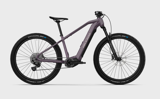 Moderni, matta violetti Helkama X 10v 27,5″ sähköpyörä *naisten suosikki* sähköinen maastopyörä, jossa on paksut nupukkarenkaat, etujousitushaarukka, levyjarrut ja pienempi runkokoko optimoidun istuvuuden saavuttamiseksi, on kuvattu valkoisella taustalla.