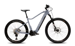 Harmaa Helkama XE12 12v 29/27,5″ 708Wh sähköpyörä, jossa on paksut nastarenkaat, etujousitushaarukka, levyjarrut ja runkoon integroitu akku, näkyy sivulta valkoisella pohjalla.