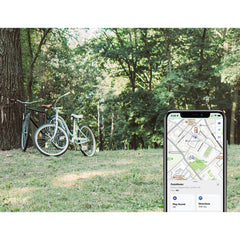 Kaksi polkupyörää on pysäköity puiston nurmikolle puiden viereen. Etualalla näkyy älypuhelimen karttasovelluksessa SÄHKÖPYÖRÄT.NET Pedalfinder pyörän GPS-paikannin, mahdollisesti Applen Etsi -verkko näyttää pyörien sijainnin.