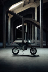 A Stark Varg SM *korkotarjous alkaen 1,99%* sähkömoottoripyörä seisoo ajovalo päällä tyhjän, varjoisan betonirakennelman keskellä tukipilareiden ja ylätasanteiden ympäröimänä.