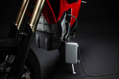 Lähikuva Stark Varg SM *korkotarjous alkaen 1,99 %* sähkömoottoripyörä Starkilta, lataus hopeisella laturirasialla ja kaapelilla tummaa taustaa vasten.