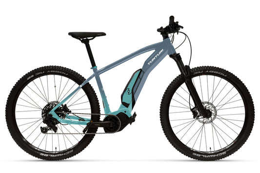 SÄHKÖPYÖRÄT.NETin sinimustassa Tunturi E290 2025 sähkömaastopyörässä on paksut renkaat, vankka runko ja Shimano E7000 -moottori alaputkessa, kuvassa profiilissa valkoista taustaa vasten.